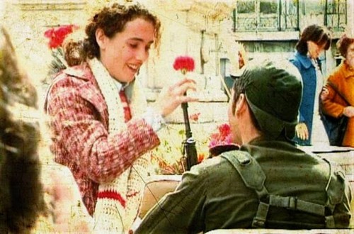 Jovem mulher oferecendo um cravo a militar no dia 