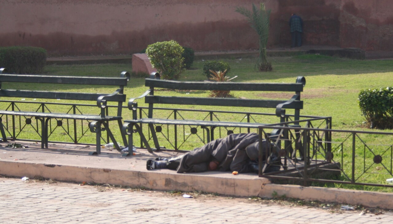 Homeless_man_sleeping_under_a_bench.jpg
